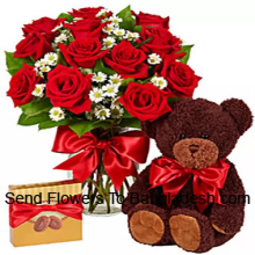 12 punaista ruusua lasimaljakossa, muutamia saniaisia, suloinen 14 tuuman pituinen teddykarhu ja tuotu suklaarasia