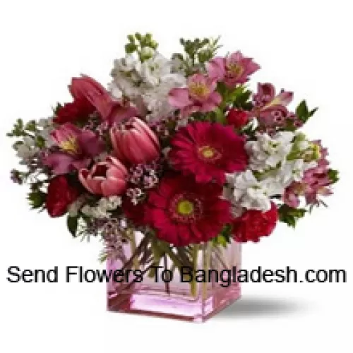 Rosas vermelhas, tulipas vermelhas e flores variadas com complementos sazonais dispostos lindamente em um vaso de vidro