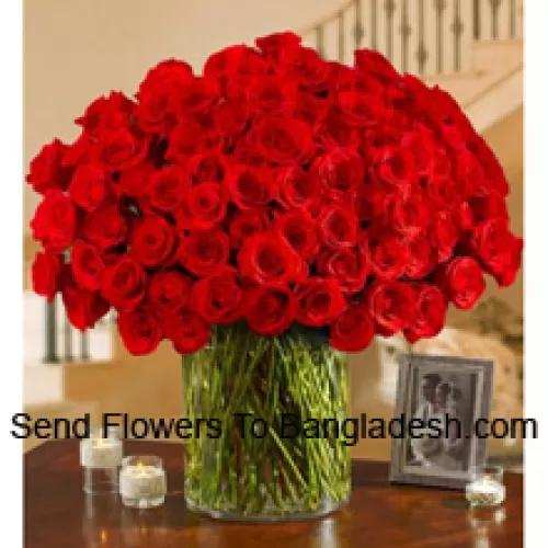100 rode rozen met wat varens in een grote glazen vaas