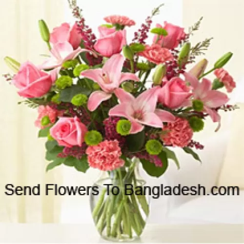 Różowe róże, różowe goździki i różowe lilie z różnymi paprociami i wypełniaczami w szklanej wazonie