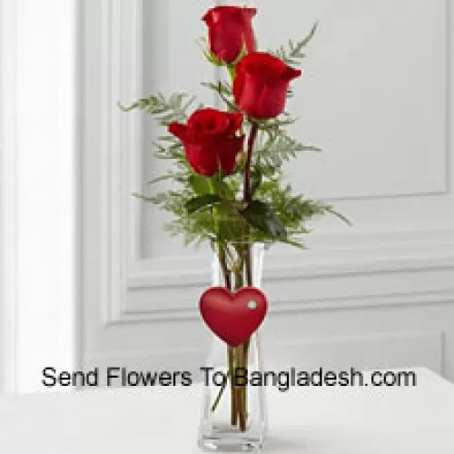 3 Trandafiri roșii într-un vas de sticlă având o mică inimioară atașată