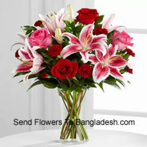 Rode en roze rozen met roze lelies en seizoensvullers in een glazen vaas